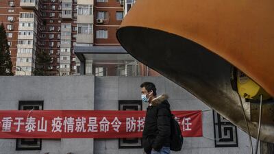 A Chinese man wears a protective mask as he walks by a banner related to the coronavirus outbreak on a residential building in Beijing. Getty Image