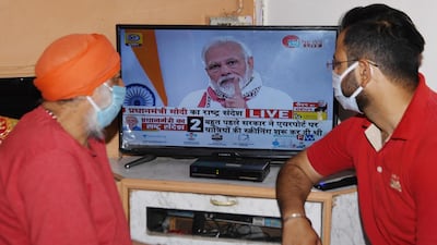 Residents wearing face masks watch Mr Modi's address to the nation r. AFP