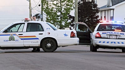 An officer takes cover behind his car in Moncton, New Brunswick. Three police officers were shot dead and two more were wounded police said as they conducted a manhunt for a man carrying a rifle and wearing camouflage clothes. Ron Ward / Moncton Times & Transcript / Reuters