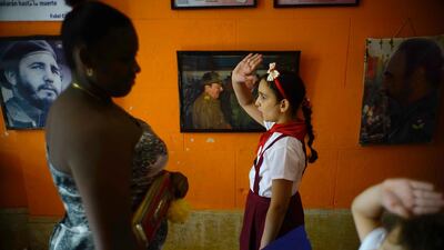 Back-dropped with pictures of the late Fidel Castro and President Raul Castro a school girl and boy raise their hands to confirm a vote as a woman casts her ballot for municipal elections in Havana, Cuba. Ramon Espinosa / AP Photo