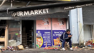 Abdelkader Al Alloush, owner of the Sham Supermarket, sits outside his shop in Belfast, Northern Ireland, after rioters set it on fire. PA via AP