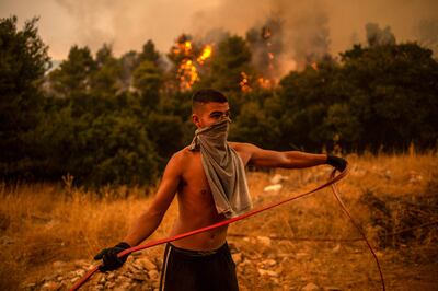 A volunteer holds a hosepipe during efforts to extinguish a fire in the village of Villa, Athens, on August 18. AFP