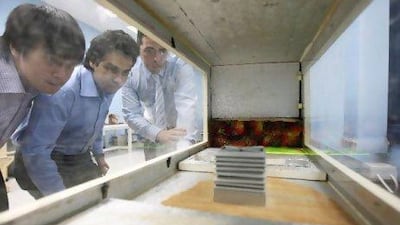 Left to right: John Calautit and Hassam Chaudhry, students of Heriot-Watt University, with Dr. Ben Hughes, watch the wind-powered air conditioning system in a campus lab in Dubai.