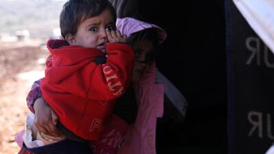 A displaced Syrian girl from the south of Aleppo province carries a baby outside their wet tent due to rain at a camp in Kafr Dariyan situated at a short distance from Syria's border with Turkey, in Idlib. AFP