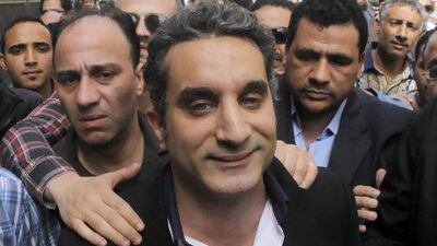 A bodyguard secures popular Egyptian television satirist Bassem Youssef, who has come to be known as Egypt's Jon Stewart, as he enters Egypt's state prosecutors office to face accusations of insulting Islam and the country's Islamist leader.