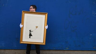 An employee of auction house Christie's poses with 'Girl with Balloon' by British artist Banksy in London. Start-ups that allow investors to buy a tiny stake in paintings by world-class artists has seen a surge in demand during the pandemic. AFP