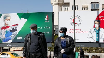 Syrians wearing face masks walk in front of posters informing about the novel coronavirus, in the capital Damascus. AFP