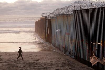 A woman walks on the beach next to the border wall topped with razor wire in Tijuana, Mexico. Courtesy: Gregory Bull