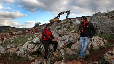 Lebanese villagers smoke shisha as Israeli soldiers work near the border. AP Photo