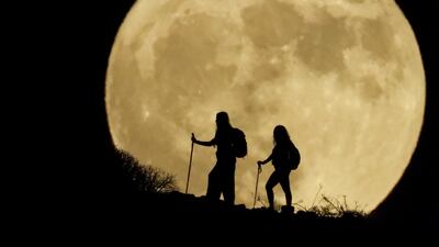 Two women walk up a mountain on Spain's Gran Canaria with the sturgeon moon in the background. Reuters