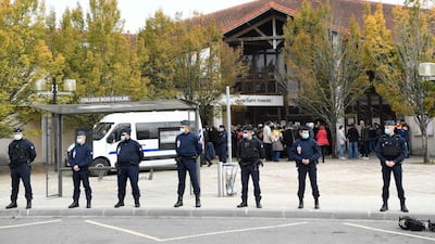 French CRS police officers stand as adults and children gather in front of flowers displayed at the entrance of a middle school in Conflans-Sainte-Honorine, 30kms northwest of Paris, on October 17, 2020, after a teacher was decapitated by an attacker who has been shot dead by policemen. The man suspected of beheading on October 16 ,2020 a French teacher who had shown his students cartoons of the prophet Mohammed was an 18-year-old born in Moscow and originating from Russia's southern region of Chechnya, a judicial source said on October 17. Five more people have been detained over the murder on October 16 ,2020 outside Paris, including the parents of a child at the school where the teacher was working, bringing to nine the total number currently under arrest, said the source, who asked not to be named. The attack happened at around 5 pm (1500 GMT) near a school in Conflans Saint-Honorine, a western suburb of the French capital. The man who was decapitated was a history teacher who had recently shown caricatures of the Prophet Mohammed in class. / AFP / Bertrand GUAY