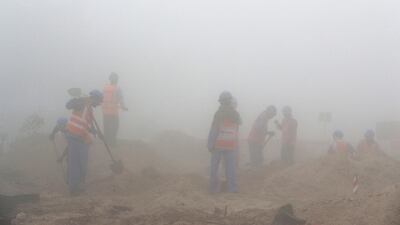 Labourers working during the early morning fog in Discovery Gardens. Pawan Singh / The National.