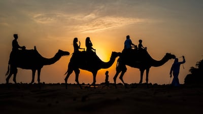 Tourists ride camels at a desert resort in Dubai at sunset. AFP