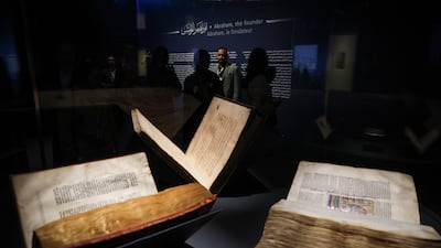 People inspect a Quran, a Torah and a Bible, part of the Letters of Light exhibition at Louvre Abu Dhabi on Monday. EPA