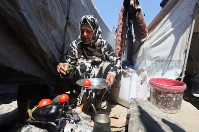 A displaced Palestinian woman cooks over a wood fire outside her tent in Khan Younis. Reuters