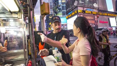 Mohammed Omar, originally from Egypt, gives a customer directions at his halal food cart during Ramadan on the corner of 42nd Street and Broadway in Times Square in New York. Michael Kirby Smith for The National