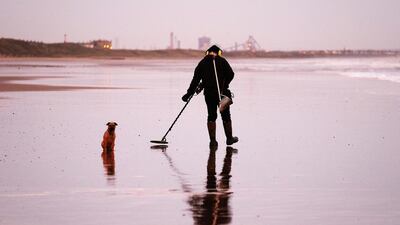 A man with a metal detector sweeps the beach at dawn in Saltburn-by-the-Sea, England. Ian Forsyth / Getty Images