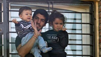 Uruguay’s striker Luis Suarez, banned from football for four months after biting an opponent at the World Cup, holds his children Benjamin and Delfina as he greets fans from his mother’s home in Lagomar, in the department of Canelones, near Montevideo, on June 27, 2014. Suarez, 27, returned home to a hero’s welcome from hundreds of fans at Montevideo airport early Friday. Uruguay’s President Jose Mujica went to the airport intending to greet the star striker, but left because Suarez’s flight was delayed. AFP PHOTO/Pablo BIELLI