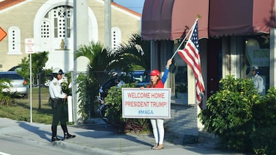 A supporter holds a signs and a flag cheering for Donald Trump after his arrival in West Palm Beach, Florida on April 18, 2019. / AFP / Nicholas Kamm