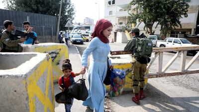 epa07927544 A woman walks past Israeli soldiers at a checkpoint in the West Bank city of Hebron, 17 October 2019. EPA/ABED AL HASHLAMOUN