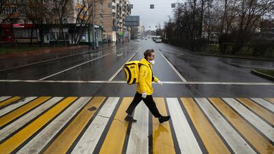 In this photo taken on Thursday, April 16, 2020, Russian businessman Sergey Nochovnyy wearing a face mask to protect against coronavirus crosses a road, on his way to pick up a food order to deliver, in Moscow, Russia. AP