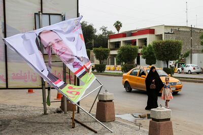 An Iraqi woman and a girl walk past an electoral banner for former Prime Minister Nouri Al Maliki that was damaged by a storm the day before, in the capital Baghdad on April 28, 2018. Sabah Arar / AFP Photo
