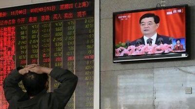 An investor sits in front of an electronic board displaying stock market information and a screen showing Chinese president Hu Jintao delivering a speech at the National Congress of the Communist Party of China.