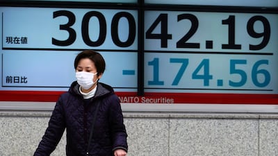 A woman wearing a mask walks in front of an electronic board showing a drop in the value of Japan's Nikkei 225 index in Tokyo on Friday. AP Photo