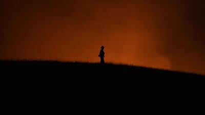 A firefighter keeps watch while a hill burns beside a housing estate, as the Thomas wildfire continues to burn in Ojai, California. Mark Ralston / AFP