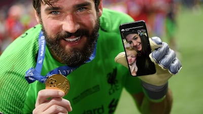 Alisson of Liverpool celebrates with his phone on the pitch after helping his side become winners. Getty