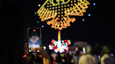 A Syrian woman takes a picture of the new national emblem of Syria, depicting an eagle inspired by ancient motifs at Palmyra carrying 14 feathers symbolising the country's 14 governorates and surmounted by three stars from the national flag, during a drone show at Ummayad Square in Damascus. AFP
