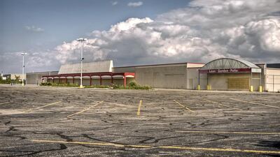 An empty, vacant commercial store with overgrown weeds and empty parking lot in the foreground. istockphoto.com