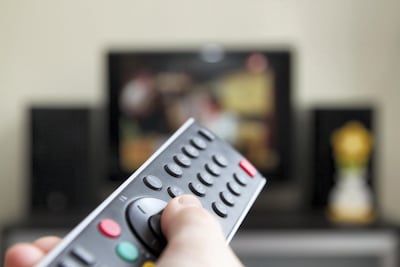 A person holding a remote in front of a television. Getty Images