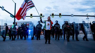 A man carrying Mexican and American flags walks in front of police during a march against immigration and customs enforcement in Denver, Colorado. AFP