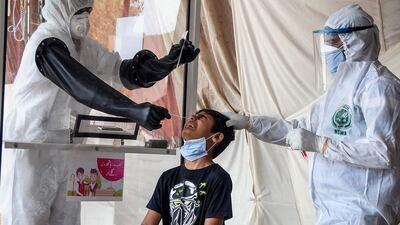 Health officials wearing protective gear take a nasal swab sample from a young boy in Karachi. AFP