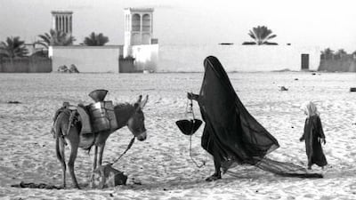Trucial Oman States, Abu Dhabi. A woman collects water outside the fort. In the background are wind towers. Ronald Codrai / TCA Abu Dhabi
