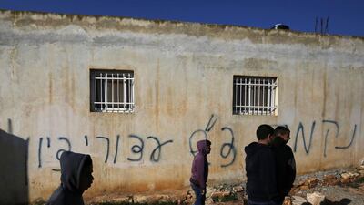 Palestinians gather next to a house sprayed with graffiti reading in Hebrew: "revenge" and "hello from the prisoners of Zion", in the village of Beitillu, near Ramallah in the Israeli occupied West Bank on December 22, 2015. Abbas Momani / AFP Photo