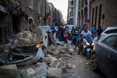 People ride past cars destroyed after a building wall collapsed following the blast. Getty Images
