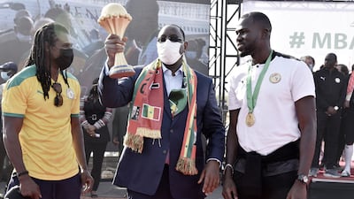 Senegal President Macky Sall, centre, holds the Africa Cup of Nations trophy flanked by Senegal coach Aliou Cisse, left, and captain Kalidou Koubaly in Dakar on Monday, February 7, 2022. AFP
