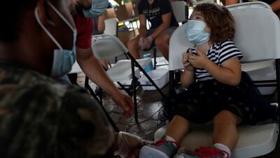 Riley Shirley, 2, smiles while wearing a face mask after receiving shoes at the Hot Springs Community Resource Fair that provided free Covid-19 vaccines, shoes, backpacks and other resources in Hot Springs, Arkansas.