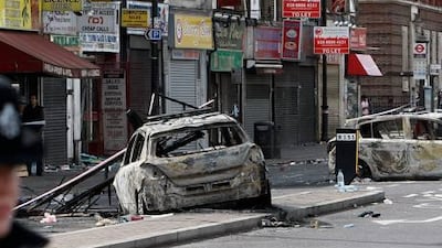 A police officer stands guard as burned police cars are seen in Tottenham, north London, on Sunday.