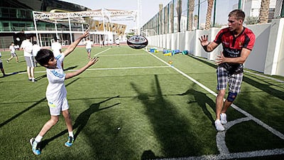 Joshua Goad from the Abu Dhabi Saracens rugby team, right, shows Ahmed Al Dhahri, left, how to pass the ball on the floodlit pitches at the Al Bateen School in Abu Dhabi.