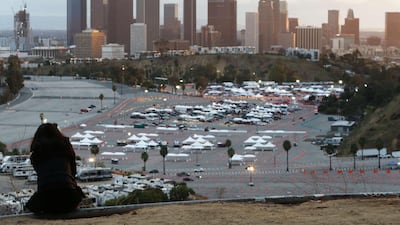 A person sits on a hillside as cars are lined up with people waiting to receive vaccines at a mass Covid-19 vaccination site at Dodger Stadium in Los Angeles, California. AFP