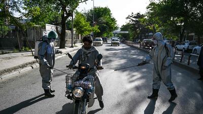 Volunteers wearing protective gear spray disinfectant on a motorist riding a motorbike, in Kabul. AFP