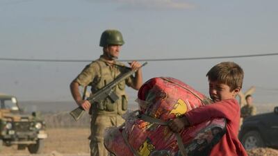 Turkish soldiers stand guard as a Syrian refugee boy carries his belongings at the border in Suruc, Turkey, on Saturday, September 20, 2014. AP Photo