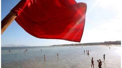 A red flag serving as a warning of shark sightings flutters over tourists enjoying a day on the beach at the Red Sea resort of Sharm el-Sheikh, Egypt.