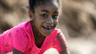 A girl covered in mud smiles as she negotiates an obstacle.