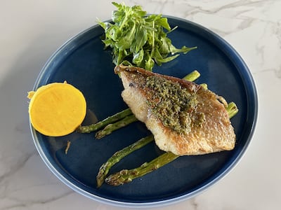 Grilled sea bass with tangy green salsa is served skin-on with asparagus, half a lemon and a simple red onion and sumac salad. Phil Johnson / The National