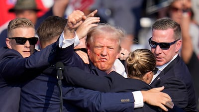 Donald Trump pumps his fist as he is helped off the stage. AP