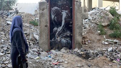 File photo of a woman walking past a mural painted by British street graffiti artist Banksy on a door of a house which was destroyed during the 2014 conflict between Israel and Hamas in the northern Gaza Strip. Mohammed Saber/EPA